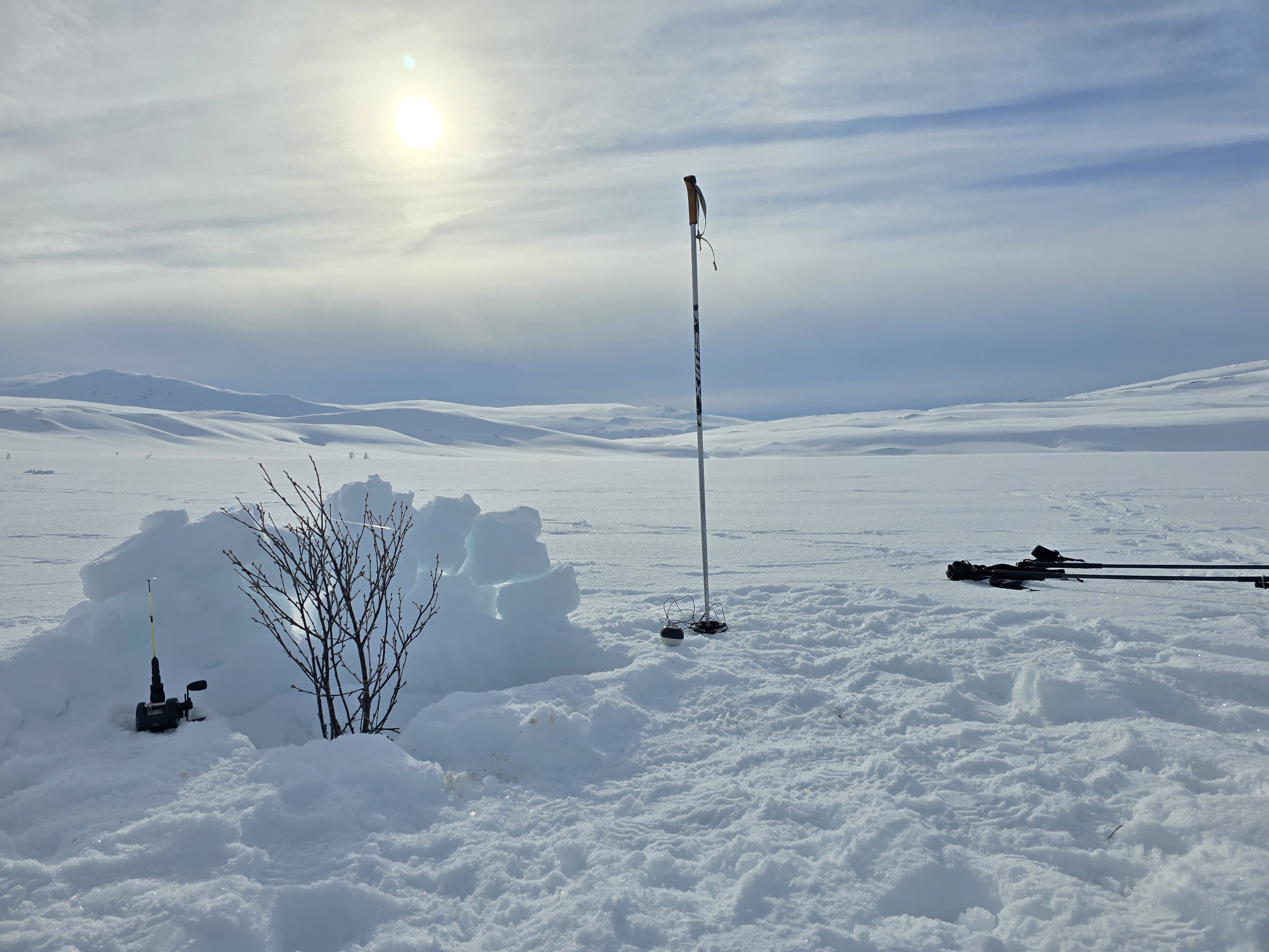 Det er vinter. En levegg av snø, et hull i isen og ei fiskestang. Det er isfiske på gang.